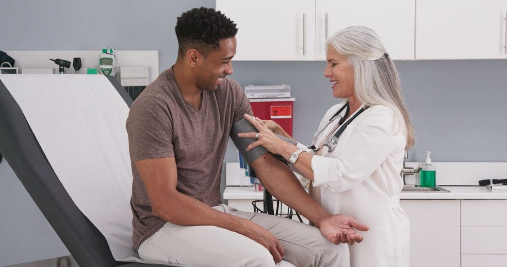 female physician checking male patients blood pressure in health clinic