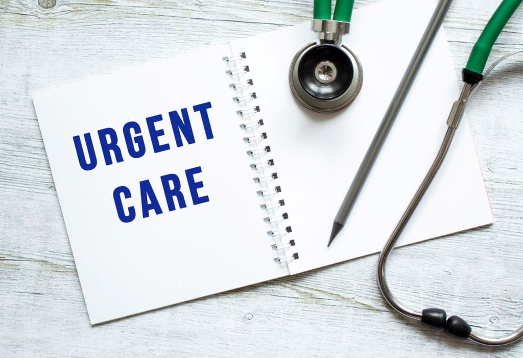 URGENT CARE is written in a notebook on a wooden table next to stethoscope.