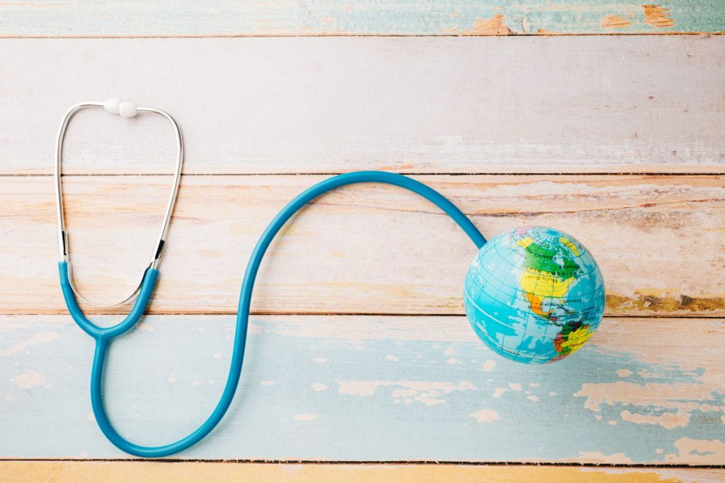 Top view blue doctor stethoscope wrapped around world globe isolated on white wood background.