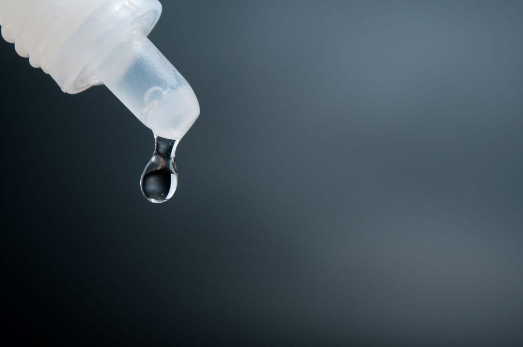 Close up of a plastic eye drop bottle with a drop of liquid